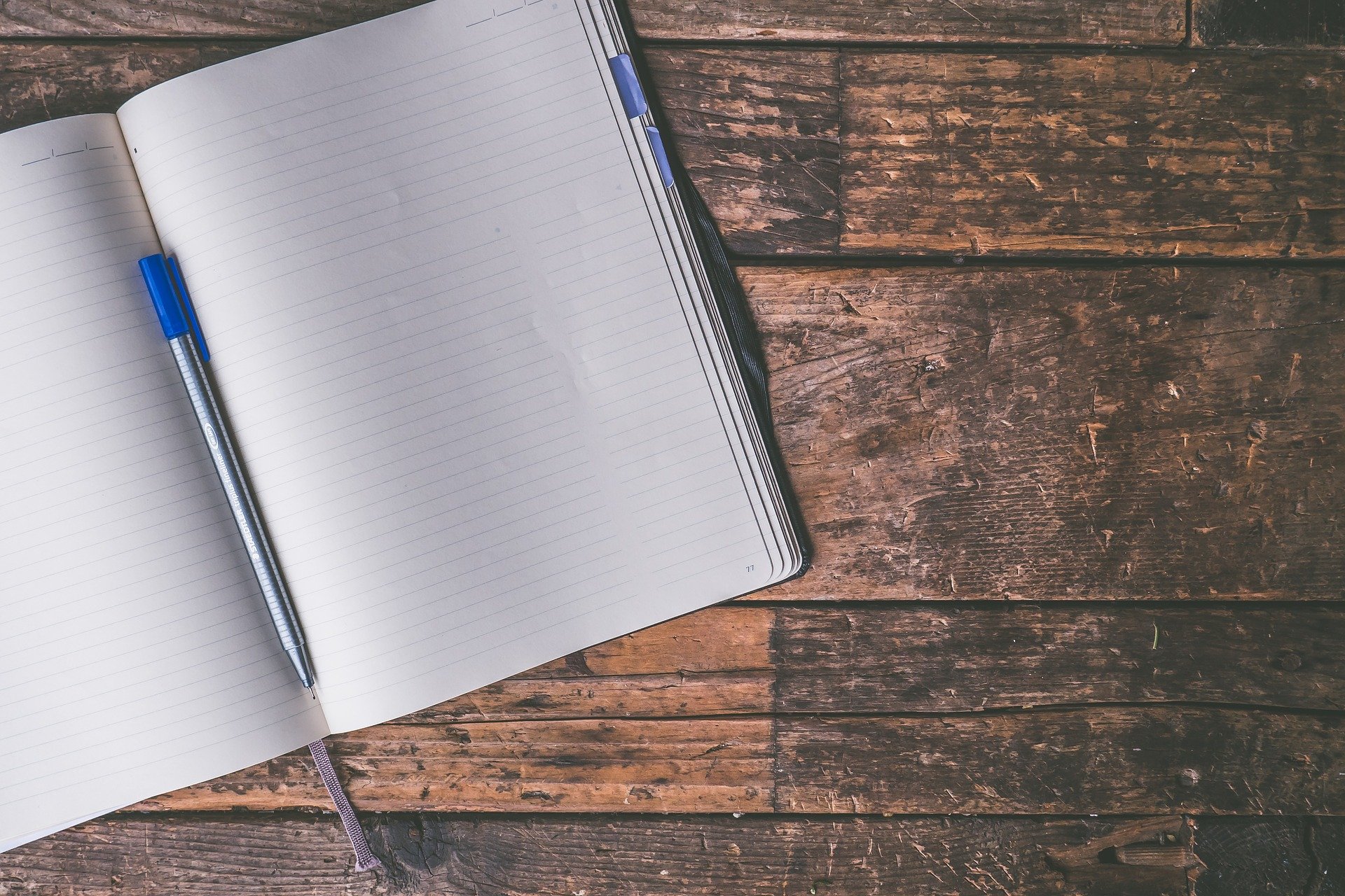 Open lined notebook with a blue pen on a rustic wooden desk