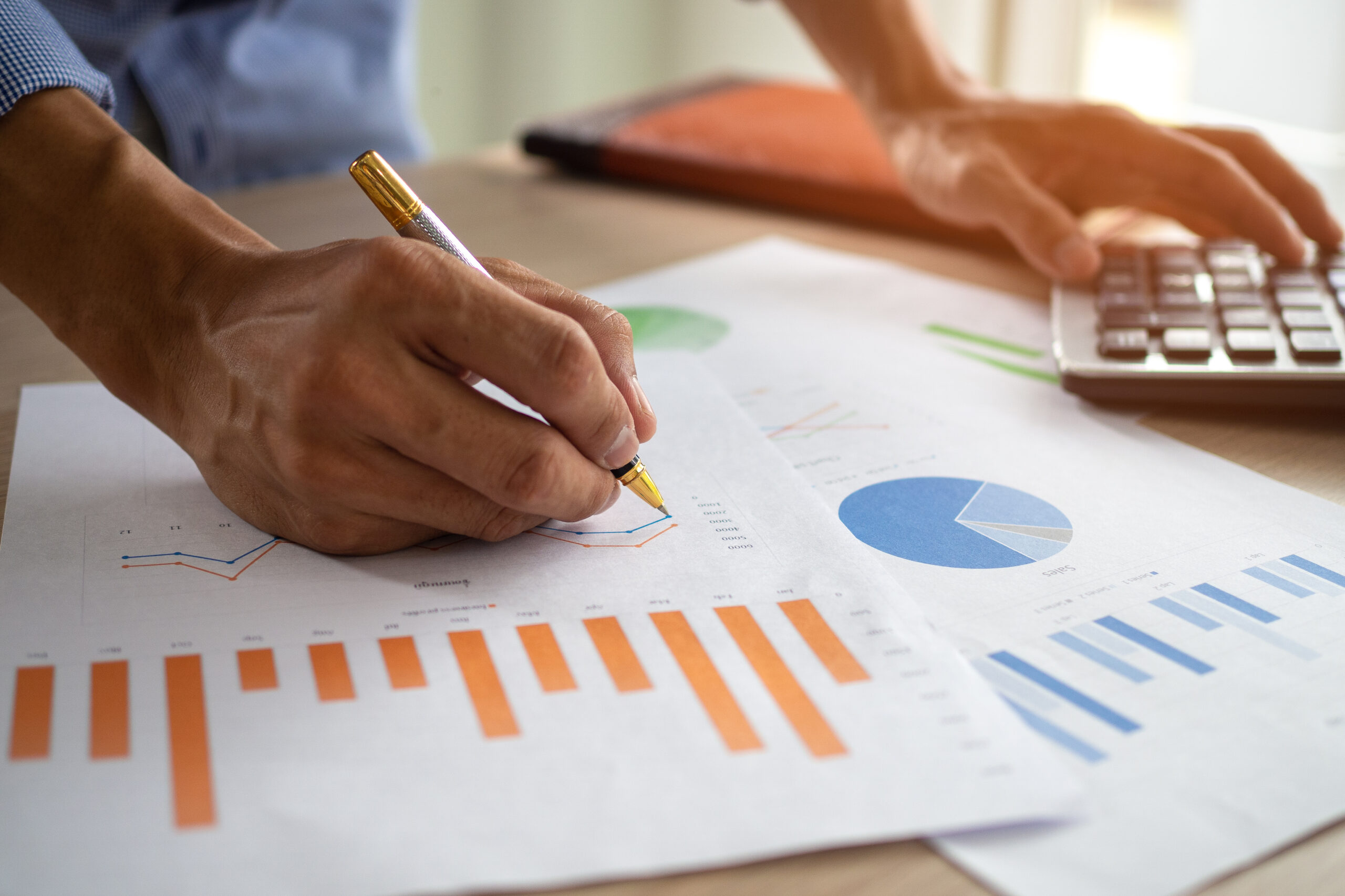 Person reviewing business charts with a pen beside a calculator