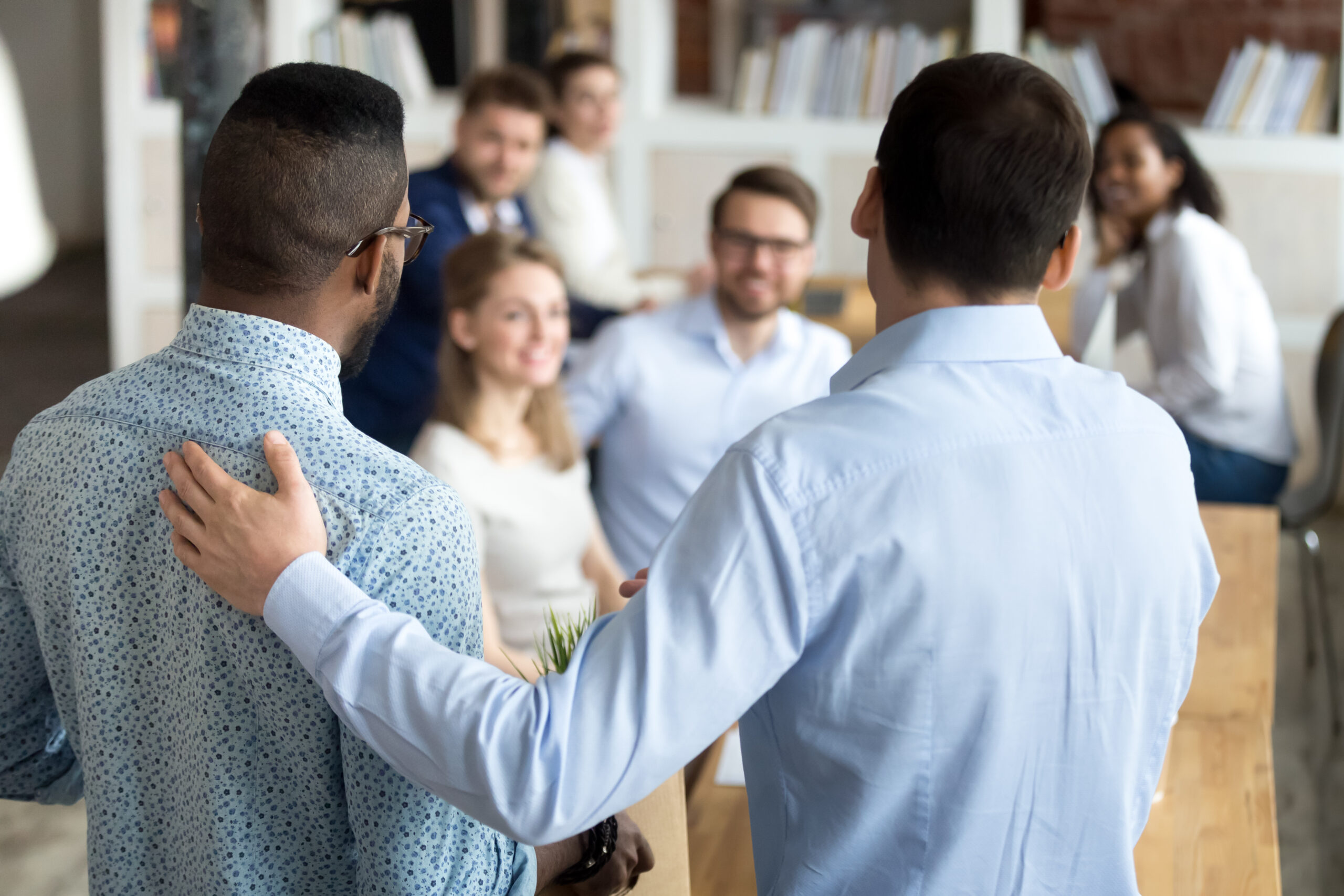 Colleagues gather in an office, with one man placing a supportive hand on another’s shoulder