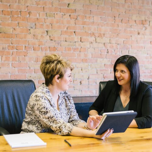 Two women discussing a tablet at a table in an office