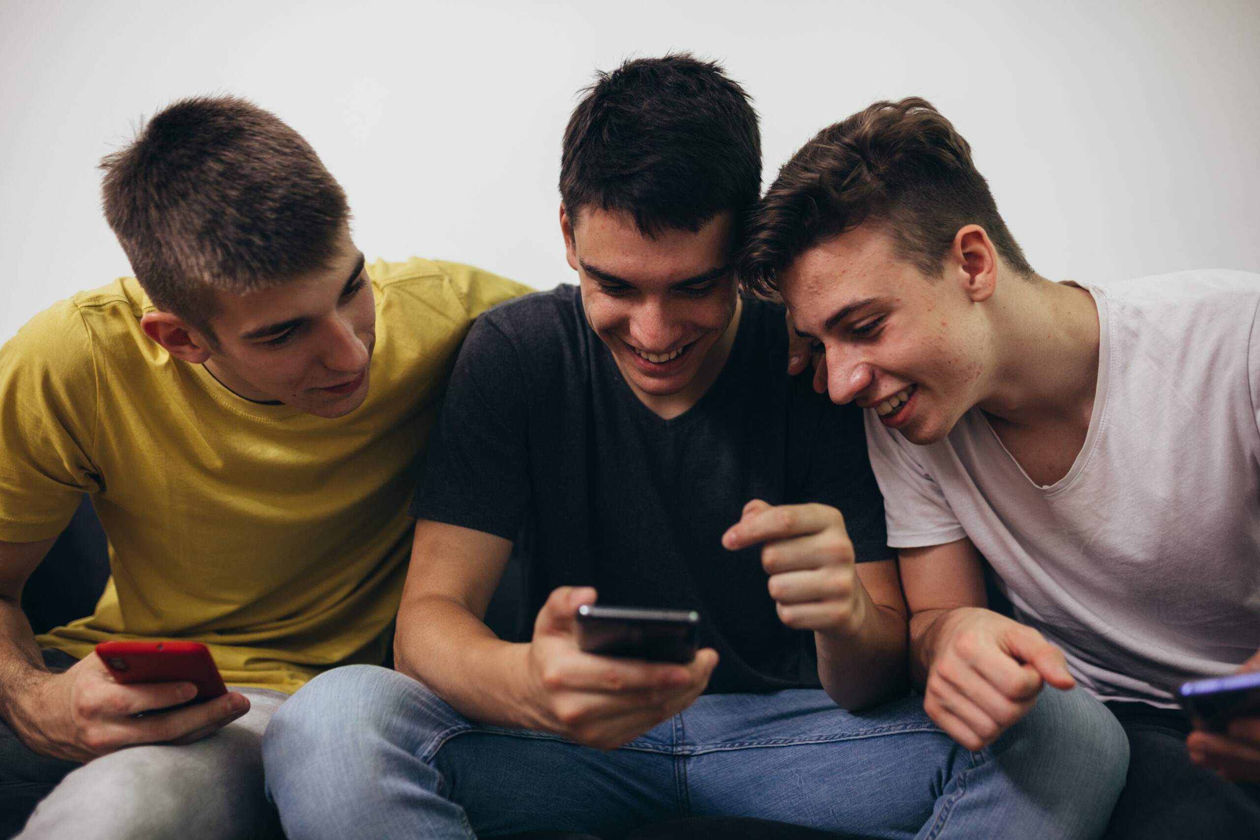 Three teenage boys laughing while looking at a phone, showing how misogyny in schools can spread through shared online content.