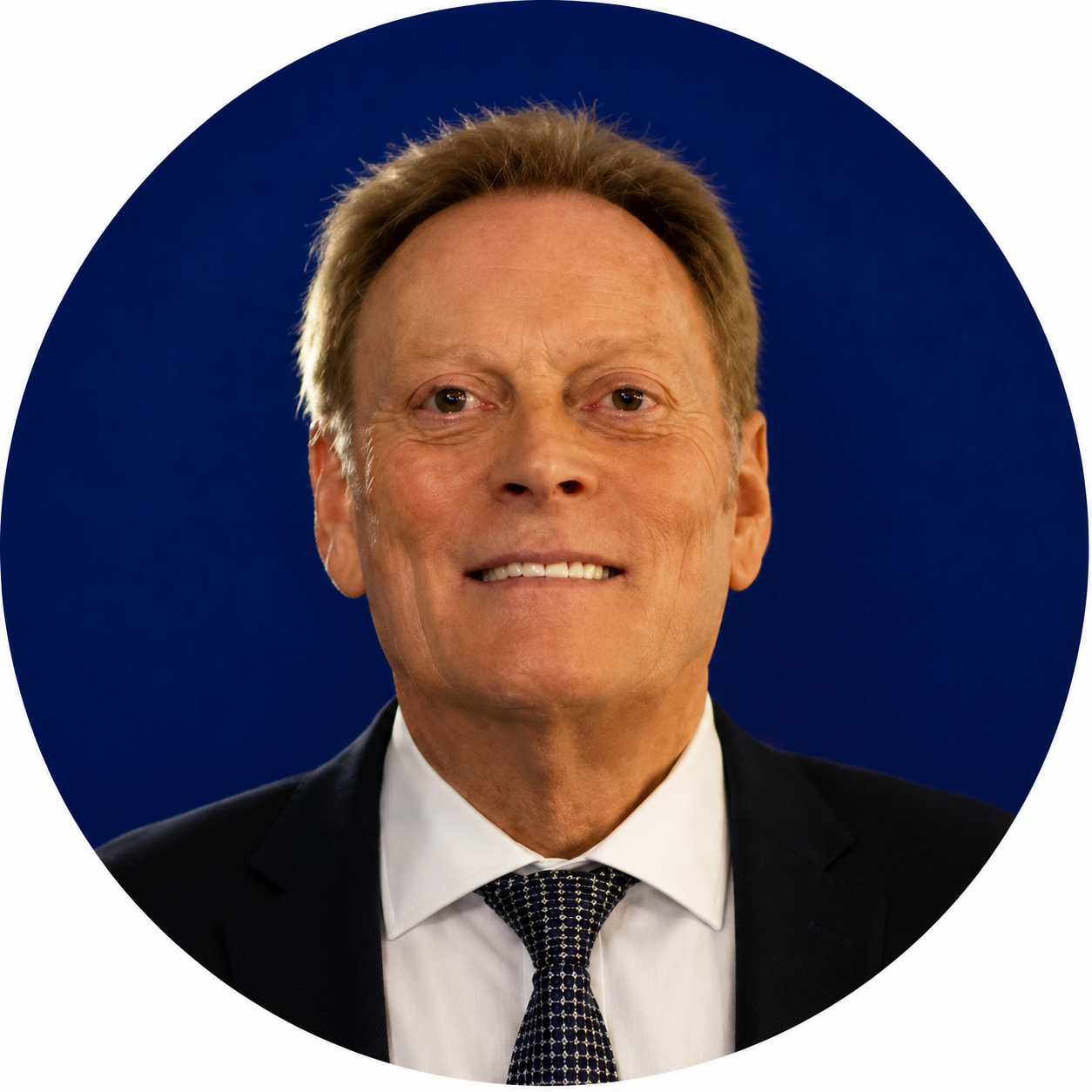 Head-and-shoulders portrait of a smiling man in a suit and patterned tie against a dark blue background