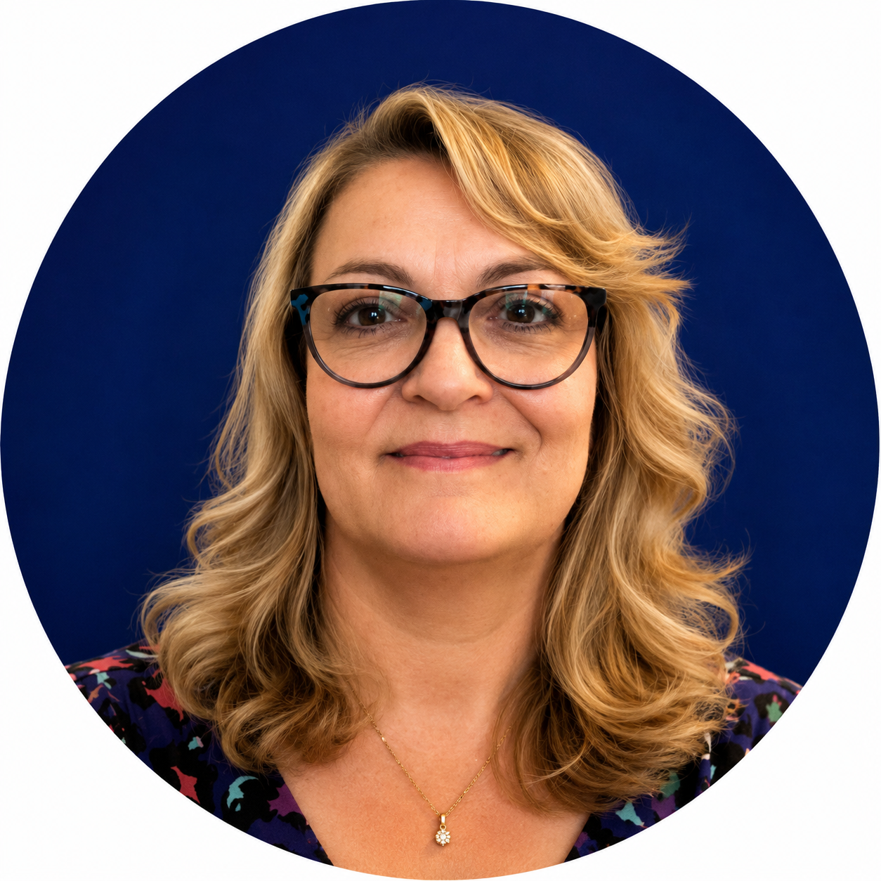 Portrait of a blonde woman wearing glasses, a floral top and a flower pendant necklace
